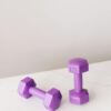 From above of purple dumbbells for fitness training placed on marble surface of table against gray background